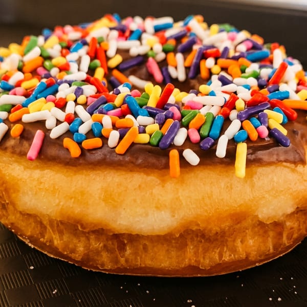 Glazed doughnut covered with colorful rainbow sprinkles on a dark textured surface.