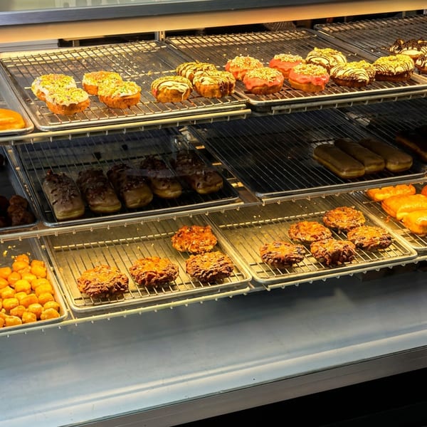 Bakery display case filled with assorted glazed donuts, pastries, fritters, and rows of freshly baked goods.