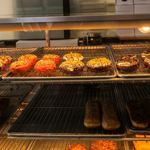 Display case filled with colorful glazed and chocolate-covered pastries arranged on metal baking trays.